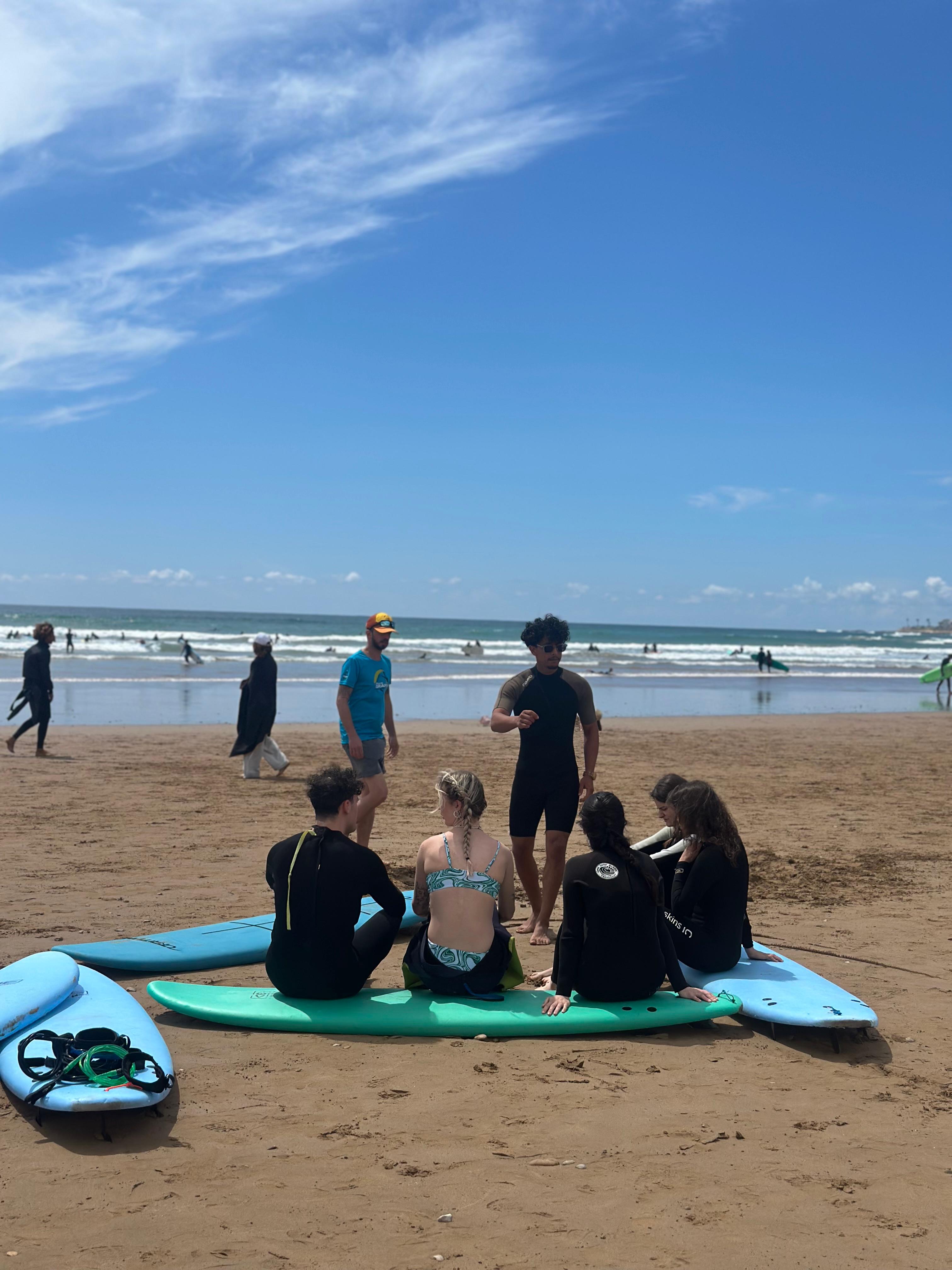 Jamal explaining surf technique to a small group seated with their boards