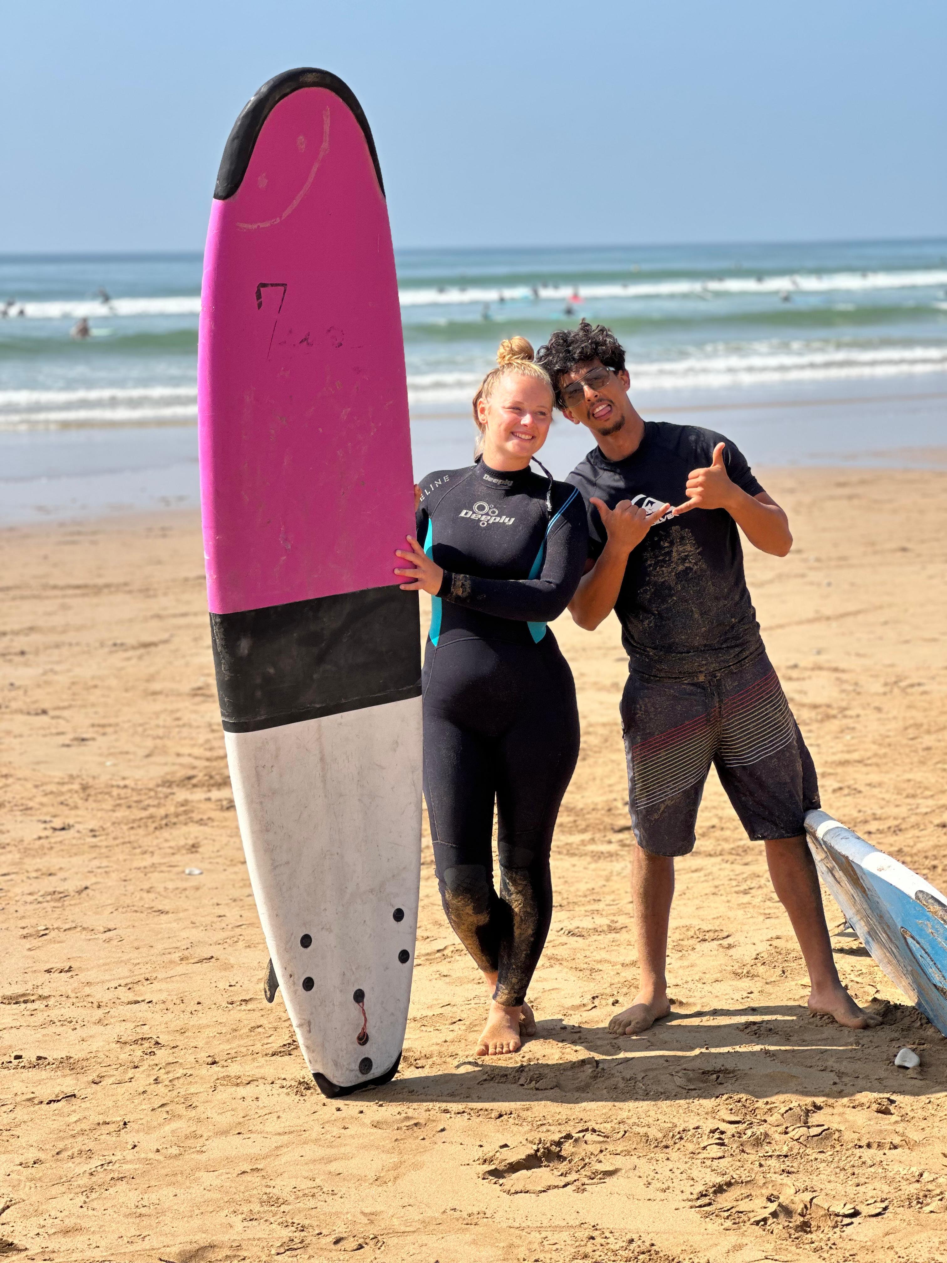 Jamal and a smiling surf guest beside a pink surfboard after a lesson